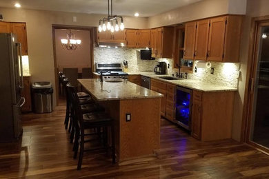 Mid-sized elegant u-shaped dark wood floor eat-in kitchen photo in Other with stainless steel appliances, an island, a double-bowl sink, raised-panel cabinets, light wood cabinets, granite countertops, white backsplash and cement tile backsplash