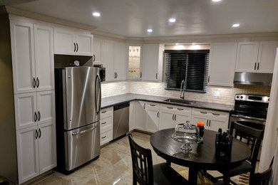 Example of a kitchen design in Toronto with a single-bowl sink, shaker cabinets, white cabinets, stainless steel appliances, black countertops and beige backsplash