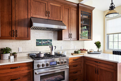 Foto de cocina clásica de tamaño medio con puertas de armario de madera oscura, salpicadero beige, salpicadero de azulejos tipo metro, electrodomésticos de acero inoxidable y encimeras blancas