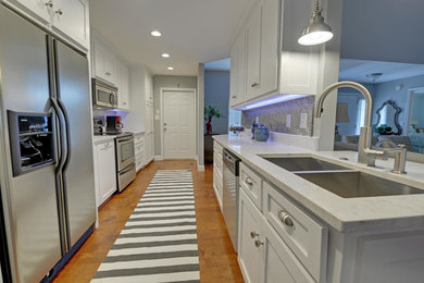 Example of a large trendy galley medium tone wood floor enclosed kitchen design in Atlanta with a double-bowl sink, shaker cabinets, white cabinets, quartzite countertops, gray backsplash, mosaic tile backsplash and stainless steel appliances