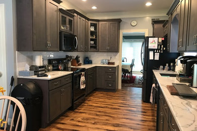 Inspiration for a mid-sized transitional l-shaped vinyl floor and brown floor eat-in kitchen remodel in Louisville with a drop-in sink, flat-panel cabinets, gray cabinets, quartz countertops, white backsplash, ceramic backsplash, black appliances, no island and white countertops