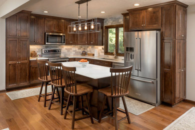 Mid-sized elegant u-shaped medium tone wood floor and brown floor eat-in kitchen photo in Columbus with an undermount sink, recessed-panel cabinets, dark wood cabinets, quartz countertops, white backsplash, marble backsplash, stainless steel appliances, an island and white countertops