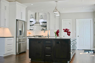 Large transitional dark wood floor and brown floor eat-in kitchen photo in Raleigh with a farmhouse sink, shaker cabinets, white cabinets, granite countertops, white backsplash, ceramic backsplash, stainless steel appliances, an island and gray countertops