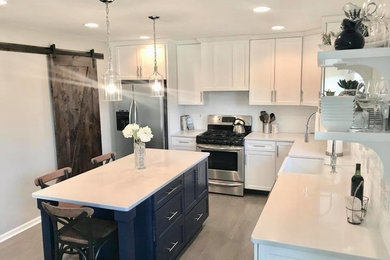 Enclosed kitchen - mid-sized contemporary l-shaped light wood floor and gray floor enclosed kitchen idea in Philadelphia with a farmhouse sink, shaker cabinets, white cabinets, quartz countertops, white backsplash, porcelain backsplash, stainless steel appliances, an island and white countertops