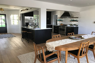 Modern inredning av ett kök, med en undermonterad diskho, svarta skåp, bänkskiva i kvartsit, vitt stänkskydd, stänkskydd i keramik, rostfria vitvaror, ljust trägolv och en köksö