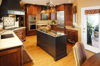 Example of a mid-sized classic galley medium tone wood floor eat-in kitchen design in Other with an undermount sink, beaded inset cabinets, dark wood cabinets, quartz countertops, beige backsplash, porcelain backsplash, stainless steel appliances and an island