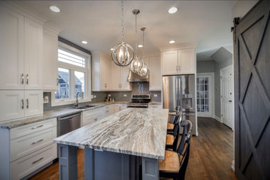 Inspiration for a large craftsman l-shaped medium tone wood floor and brown floor eat-in kitchen remodel in Austin with an undermount sink, recessed-panel cabinets, white cabinets, granite countertops, gray backsplash, porcelain backsplash, stainless steel appliances, an island and beige countertops