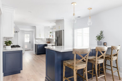 Inspiration for a mid-sized coastal u-shaped light wood floor and beige floor kitchen remodel with a farmhouse sink, shaker cabinets, blue cabinets, quartzite countertops, stone slab backsplash, stainless steel appliances, a peninsula, white backsplash and white countertops