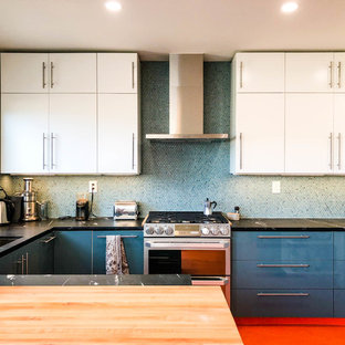 Inspiration pour une cuisine design en U de taille moyenne avec un évier encastré, un placard à porte plane, une crédence bleue, un électroménager en acier inoxydable, un sol en linoléum, une péninsule, des portes de placard bleues, une crédence en mosaïque, un sol rouge, un plan de travail noir et un plan de travail en granite.