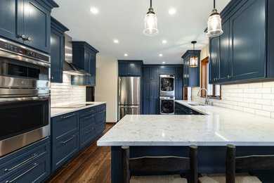 Mid-sized farmhouse l-shaped dark wood floor and brown floor eat-in kitchen photo in New York with an undermount sink, shaker cabinets, blue cabinets, quartz countertops, white backsplash, subway tile backsplash, stainless steel appliances, a peninsula and white countertops