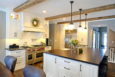 Mid-sized country single-wall dark wood floor and brown floor eat-in kitchen photo in Milwaukee with a farmhouse sink, shaker cabinets, white cabinets, wood countertops, white backsplash, subway tile backsplash, stainless steel appliances, an island and brown countertops