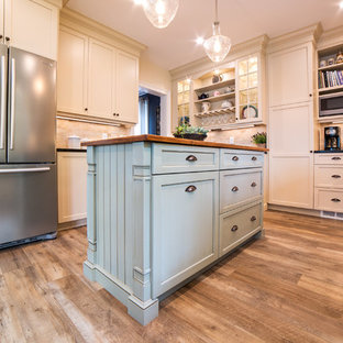 Mid-sized traditional separate kitchen in New York with a farmhouse sink, recessed-panel cabinets, beige cabinets, soapstone benchtops, beige splashback, travertine splashback, stainless steel appliances, vinyl floors, with island, brown floor and black benchtop.