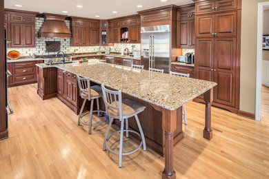 Example of a large classic l-shaped light wood floor and beige floor eat-in kitchen design in Other with a double-bowl sink, raised-panel cabinets, medium tone wood cabinets, granite countertops, beige backsplash, ceramic backsplash, stainless steel appliances, an island and beige countertops
