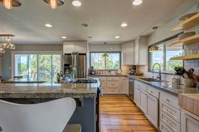 Example of a large trendy galley light wood floor open concept kitchen design in Sacramento with an undermount sink, recessed-panel cabinets, white cabinets, granite countertops, white backsplash, ceramic backsplash, stainless steel appliances and a peninsula