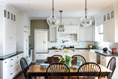 Example of a large transitional u-shaped medium tone wood floor open concept kitchen design in Chicago with a farmhouse sink, shaker cabinets, white cabinets, white backsplash, stone tile backsplash, stainless steel appliances and an island