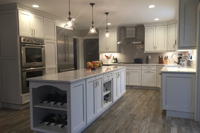 Bild på ett stort lantligt kök, med en rustik diskho, luckor med infälld panel, vita skåp, bänkskiva i kvarts, grått stänkskydd, stänkskydd i keramik, rostfria vitvaror, klinkergolv i porslin och en köksö