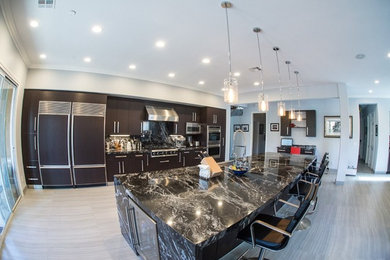 Example of a large minimalist galley ceramic tile open concept kitchen design in Las Vegas with a single-bowl sink, flat-panel cabinets, dark wood cabinets, granite countertops, stainless steel appliances and an island