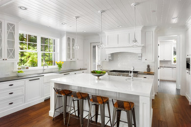 Kitchen - mid-sized transitional u-shaped medium tone wood floor kitchen idea in Los Angeles with recessed-panel cabinets, white cabinets, marble countertops, white backsplash, subway tile backsplash, an island, a farmhouse sink and paneled appliances