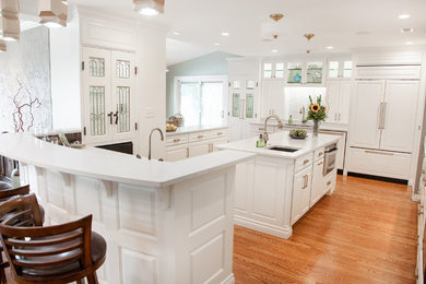 Medium sized traditional u-shaped kitchen/diner in Wichita with a submerged sink, raised-panel cabinets, white cabinets, ceramic splashback, integrated appliances, an island, composite countertops, white splashback, medium hardwood flooring and brown floors.