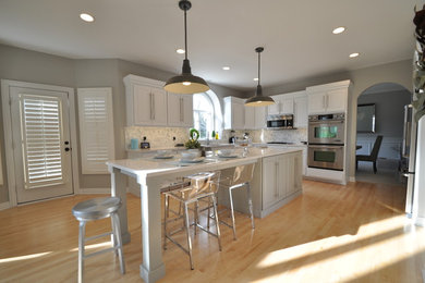 Eat-in kitchen - mid-sized transitional light wood floor eat-in kitchen idea in Chicago with a farmhouse sink, white cabinets, quartz countertops, white backsplash, mosaic tile backsplash, stainless steel appliances and an island