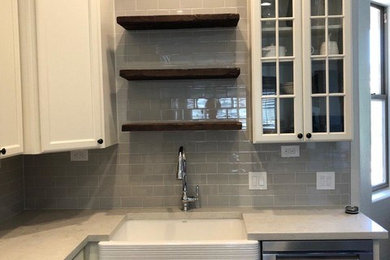 Inspiration for a mid-sized laminate floor and brown floor kitchen remodel in Phoenix with a farmhouse sink, white cabinets, granite countertops, gray backsplash, porcelain backsplash, stainless steel appliances, an island and white countertops