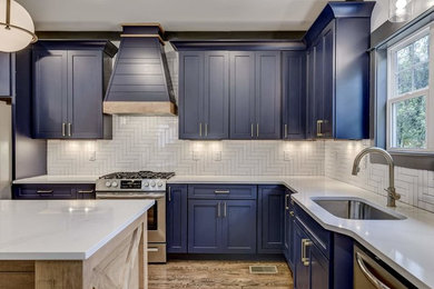 ローリーにある中くらいなモダンスタイルのおしゃれなコの字型キッチン (ドロップインシンク、青いキャビネット、白いキッチンパネル、シルバーの調理設備、茶色い床、マルチカラーのキッチンカウンター) の写真