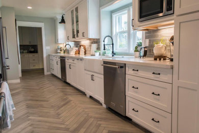 Example of a large transitional galley light wood floor and gray floor enclosed kitchen design in Los Angeles with a farmhouse sink, shaker cabinets, white cabinets, gray backsplash, subway tile backsplash, stainless steel appliances, white countertops, quartz countertops and no island
