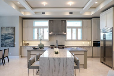 Example of a trendy l-shaped beige floor kitchen design in Miami with shaker cabinets, white cabinets, stainless steel appliances, an island and white countertops