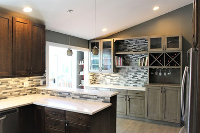 Example of a large classic u-shaped medium tone wood floor and brown floor enclosed kitchen design in Seattle with an undermount sink, recessed-panel cabinets, medium tone wood cabinets, solid surface countertops, multicolored backsplash, stone tile backsplash, stainless steel appliances, a peninsula and white countertops