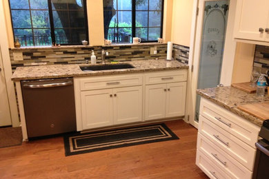 Example of a mid-sized classic l-shaped medium tone wood floor and brown floor enclosed kitchen design in Los Angeles with shaker cabinets, white cabinets, granite countertops, multicolored backsplash, matchstick tile backsplash, stainless steel appliances, no island, beige countertops and an undermount sink