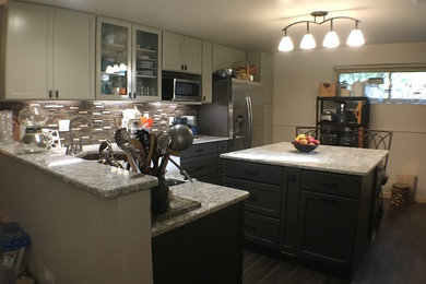 Mid-sized elegant l-shaped vinyl floor eat-in kitchen photo in Indianapolis with a farmhouse sink, recessed-panel cabinets, gray cabinets, solid surface countertops, brown backsplash, glass tile backsplash, white appliances and an island