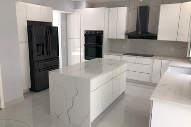 Large minimalist u-shaped porcelain tile, beige floor and tray ceiling kitchen pantry photo in Tampa with a farmhouse sink, flat-panel cabinets, white cabinets, quartz countertops, white backsplash, quartz backsplash, black appliances, an island and white countertops