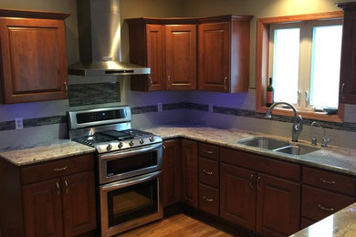 Mid-sized elegant u-shaped medium tone wood floor and brown floor kitchen photo in Milwaukee with an undermount sink, raised-panel cabinets, medium tone wood cabinets, granite countertops, white backsplash, ceramic backsplash, stainless steel appliances, no island and multicolored countertops