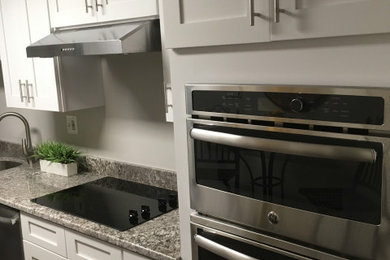 Example of a mid-sized trendy l-shaped dark wood floor and brown floor eat-in kitchen design in DC Metro with an undermount sink, shaker cabinets, white cabinets, granite countertops, stainless steel appliances, no island and gray countertops