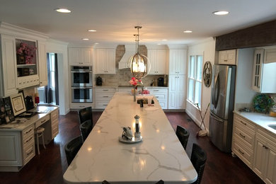 Inspiration for a large timeless u-shaped dark wood floor and brown floor enclosed kitchen remodel in Baltimore with an undermount sink, raised-panel cabinets, white cabinets, marble countertops, beige backsplash, stainless steel appliances, an island, white countertops and travertine backsplash
