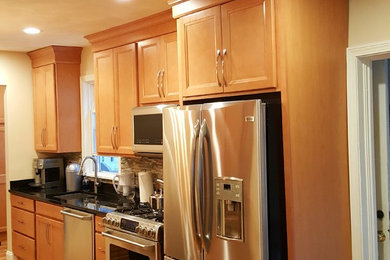 Example of a transitional light wood floor kitchen design in Boston with an undermount sink, shaker cabinets, granite countertops, glass tile backsplash, stainless steel appliances and an island