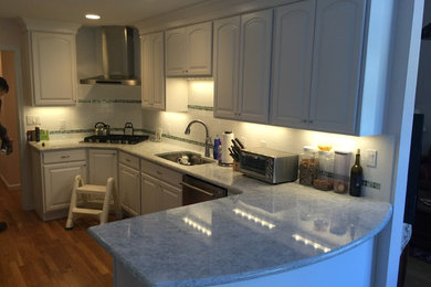 This is an example of a medium sized classic l-shaped enclosed kitchen in Boston with a single-bowl sink, raised-panel cabinets, white cabinets, engineered stone countertops, white splashback, metro tiled splashback, stainless steel appliances and light hardwood flooring.