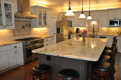 Example of a mid-sized transitional l-shaped concrete floor eat-in kitchen design in Dallas with an island, a farmhouse sink, raised-panel cabinets, white cabinets, granite countertops, beige backsplash, ceramic backsplash and stainless steel appliances