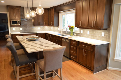 Example of a large classic u-shaped light wood floor open concept kitchen design in DC Metro with an undermount sink, raised-panel cabinets, dark wood cabinets, quartz countertops, gray backsplash, glass tile backsplash, stainless steel appliances and an island