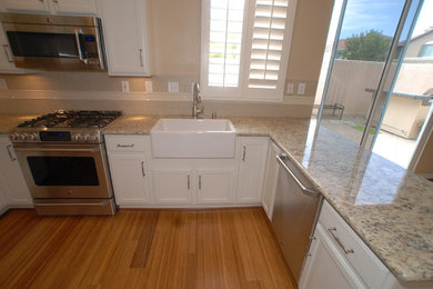 Inspiration for a small timeless u-shaped bamboo floor open concept kitchen remodel in Orange County with a farmhouse sink, recessed-panel cabinets, white cabinets, granite countertops, beige backsplash, subway tile backsplash, stainless steel appliances and a peninsula