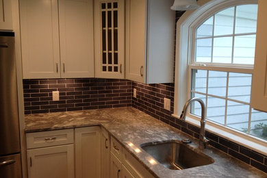 Photo of a medium sized traditional l-shaped kitchen in New York with a submerged sink, shaker cabinets, white cabinets, granite worktops, black splashback, metro tiled splashback and stainless steel appliances.