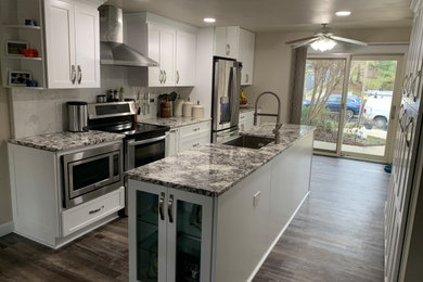 Mid-sized minimalist galley vinyl floor and brown floor kitchen pantry photo in DC Metro with an undermount sink, shaker cabinets, white cabinets, granite countertops, white backsplash, porcelain backsplash, stainless steel appliances, an island and brown countertops