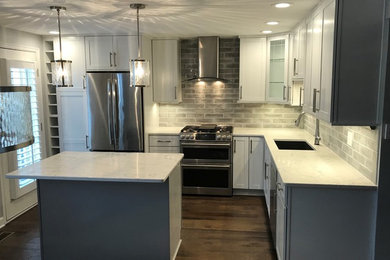 Inspiration for a mid-sized transitional l-shaped dark wood floor and brown floor eat-in kitchen remodel in Other with an undermount sink, shaker cabinets, white cabinets, quartz countertops, gray backsplash, glass tile backsplash, stainless steel appliances, an island and white countertops