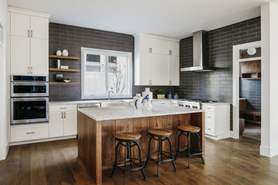 Large minimalist l-shaped medium tone wood floor, brown floor and vaulted ceiling eat-in kitchen photo in Los Angeles with a farmhouse sink, shaker cabinets, white cabinets, granite countertops, gray backsplash, subway tile backsplash, stainless steel appliances, an island and white countertops