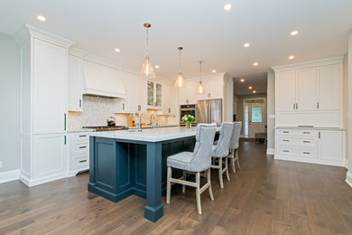Large elegant l-shaped medium tone wood floor and brown floor enclosed kitchen photo in Toronto with an undermount sink, recessed-panel cabinets, white cabinets, marble countertops, gray backsplash, mosaic tile backsplash, stainless steel appliances, an island and white countertops