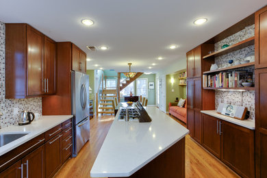 Cette photo montre une cuisine ouverte parallèle en bois brun de taille moyenne avec une crédence blanche, un électroménager en acier inoxydable, parquet clair et îlot.