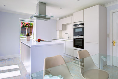 Design ideas for a medium sized contemporary galley kitchen/diner in Other with a single-bowl sink, flat-panel cabinets, grey cabinets, laminate countertops, white splashback, glass sheet splashback, black appliances, laminate floors, an island and grey floors.