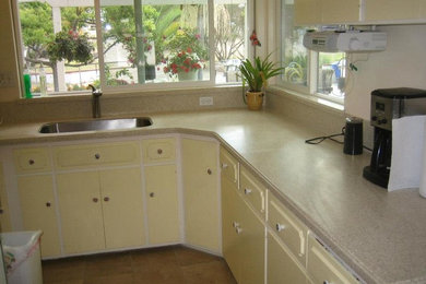 Example of a classic medium tone wood floor kitchen design in San Diego with an undermount sink, raised-panel cabinets, yellow cabinets, solid surface countertops, white backsplash, ceramic backsplash, white appliances and no island