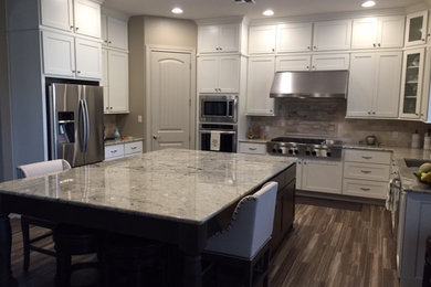 Large trendy u-shaped dark wood floor eat-in kitchen photo in Austin with a double-bowl sink, raised-panel cabinets, white cabinets, marble countertops, beige backsplash, ceramic backsplash, stainless steel appliances and an island