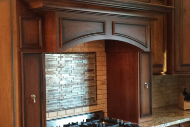Mid-sized arts and crafts u-shaped eat-in kitchen photo in Cleveland with raised-panel cabinets, dark wood cabinets, granite countertops, beige backsplash, stone tile backsplash, stainless steel appliances and an island